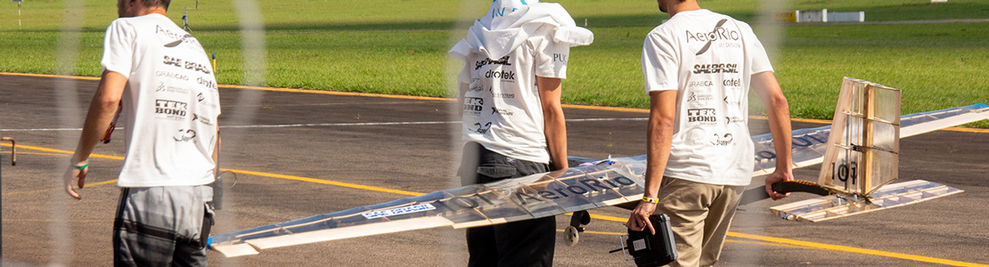 Dois membros da equipe carregando o avião, com os patrocínios nas costas da camisa em destaque.